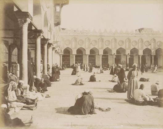 RECORD DATE NOT STATED Students in the courtyard of the Al-Azhar Mosque in Cairo, Courtyard and colonnade of the Al-Azhar Mosque, with students, photograph, Part of a travel album with 80 photos of Egypt., negative number: 1371 , photographer: Maison Bonfils, Cairo (city), c. 1870 - c. 1898, Ottoman Empire, North Africa, pasteboard, paper, albumen print, height 224 mm x width 280 mm, temple, shrine, Islam, Mohammedanism, A wide sunlit courtyard bordered by a building with a row of tall arches and decorative round medallions above each arch, and a colonnaded portico with columns and carved capitals along one side; many people wearing long robes and head coverings sit, stand, walk, or recline across the paved ground, some grouped near the columns and others scatte Copyright Penta Springs LCK260531_03304