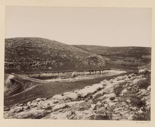 RECORD DATE NOT STATED Palestine - General view of Solomon s basins, Solomon s basin in Palestine, photograph, Part of travel album with photos of Jerusalem and other biblical places., negative number: 337 , photographer: Maison Bonfils, Palestine, c. 1867 - c. 1895, pasteboard, paper, albumen print, height 218 mm x width 283 mm, pound, pool., A wide landscape photograph shows a rocky hillside in the foreground with scattered low vegetation and rough textured stones, a terraced depression or basin carved into the middle ground with layered ledges and a shallow pool of water, sloping fields and more stony hills stretching into the distance under a pale, empty sky, and a few low stone walls and indistinct small structures dotting the distant terrain. Copyright Penta Springs LCK260621_006370