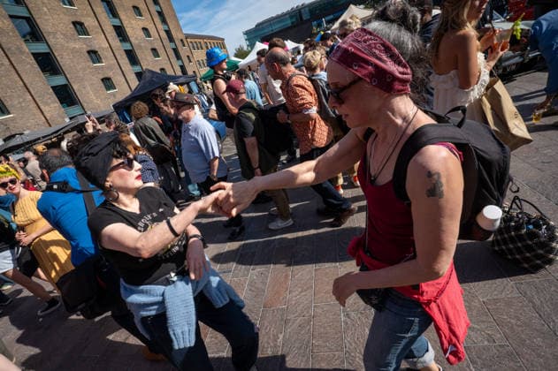 September 26, 2026, London, United Kingdom: Two attendees at the King™s Cross Classic Car Boot Sale, held at Granary Square in King™s Cross, London, hold hands and dance. The Kings Cross Classic Car Boot Sale returned to Granary Square and Stable Street, King™s Cross, London, for its 11th year. Held several times throughout the year, the event brings together vintage fashion, second-hand clothing, jewellery, homewares, collectables and vinyl records alongside classic cars, motorcycles and commercial vehicles. Visitors browsed stalls and traders, with many making a special effort to dress in period clothing inspired by the 1950s, 1960s and 1970s.continuing a tradition associated with the event. London United Kingdom - ZUMAs197 20260926_aaa_s197_385 Copyright: xJamesxWilloughbyx