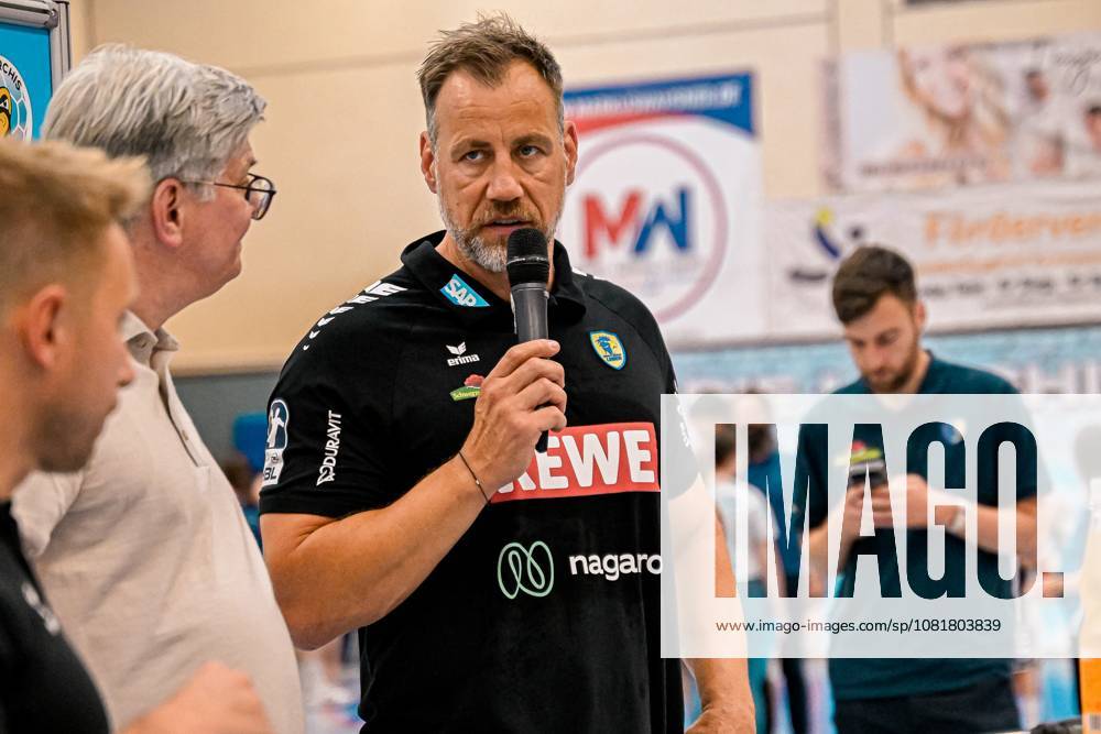 Maik Machulla, an official with the Rhein Neckar Löwen, speaks into the microphone during the DHB Cup game between the Rhein Neckar Löwen and SV Salamander Kornwestheim on August 21, 2026, at the Sporthalle Ost in Kornwestheim. The official is wearing the team’s black uniform featuring the sponsor logos of SAP, REWE, and nagaro, and addresses the spectators and team members in attendance. Maik Machulla speaks at the DHB Cup event in Kornwestheim