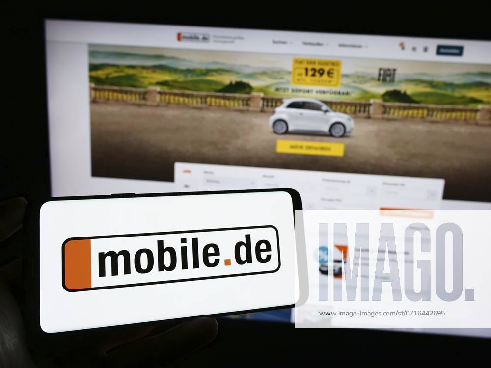 Stuttgart, Germany, 11-14-2023: Person holding mobile phone with logo of German car online marketplace company mobile.de GmbH in front of web page. Focus on phone display, Europe