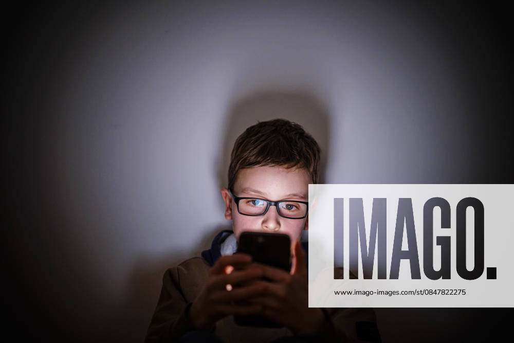 Symbol photo Staged photo on the topic of children using social media A boy sits in a dark room and is illuminated by a smartphone Berlin, 16 02 2026 Berlin Germany
