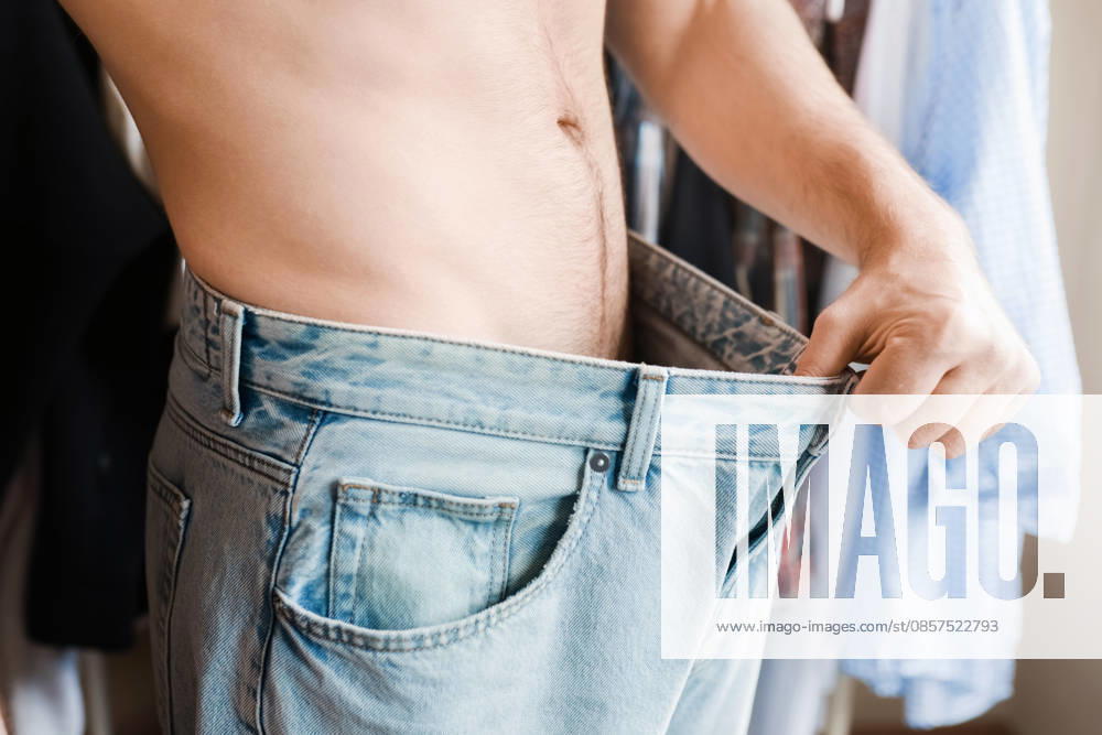 Nahaufnahme eines Mannes, der den Bund seiner übergroßen Jeans herunterzieht, um seinen Erfolg beim Abnehmen zu zeigen. Das Konzept von Körperveränderung, gesunder Ernährung und Fitnesserfolgen. Nahaufnahme eines Mannes, der den Bund seiner übergroßen Jeans herunterzieht, um seinen Erfolg beim Abnehmen zu zeigen. Das Konzept von Körperveränderung, gesunder Ernährung und Fitnesserfolgen. (License=RF) ,model released, Symbolfoto