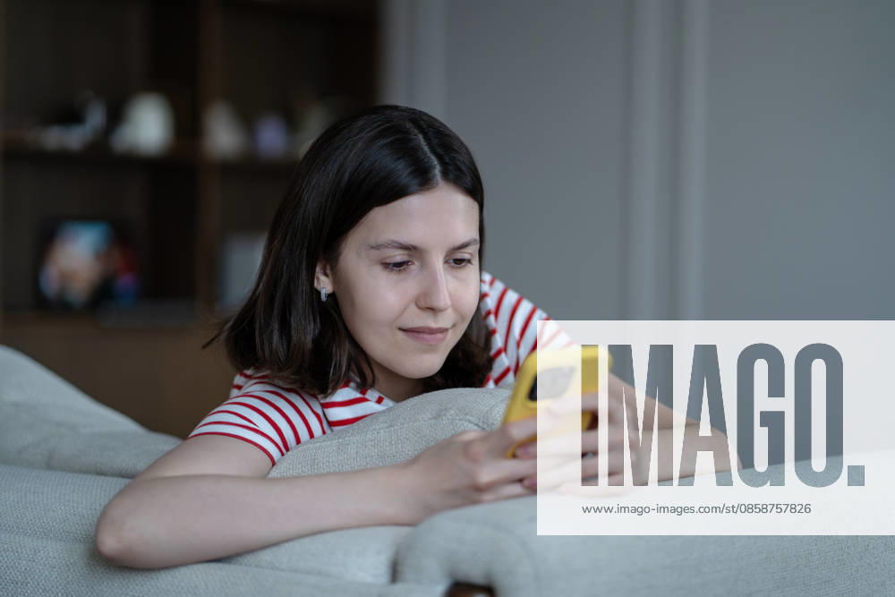Glückliches, zufriedenes Teenager-Mädchen, das in sozialen Medien scrollt oder online auf dem Telefon chattet, auf der Couch zu Hause Glückliches, zufriedenes Teenager-Mädchen, das in sozialen Medien scrollt oder online auf dem Telefon chattet, auf der Couch zu Hause (License=RF) ,model released, Symbolfoto