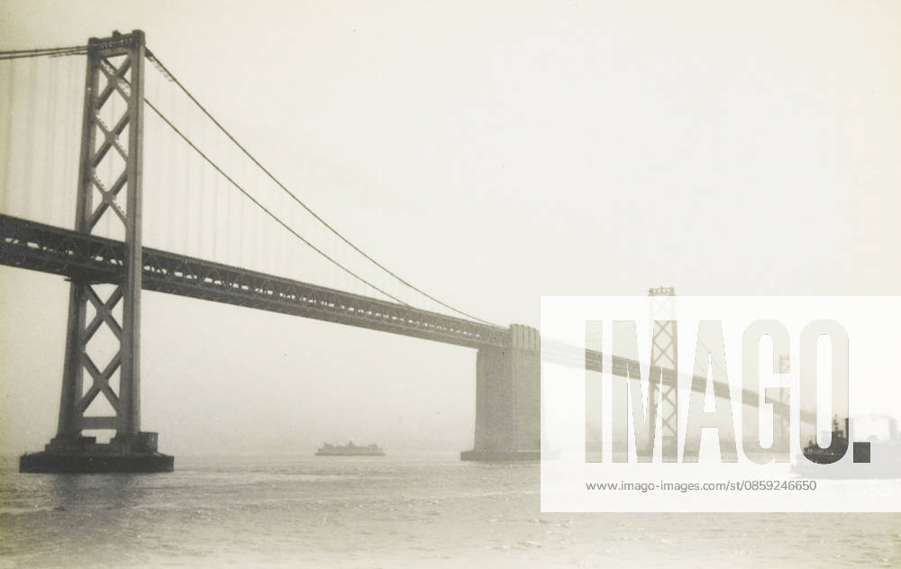 Oakland Bridge, San Francisco, photograph, title: OAKLAND BRIDGE, SAN FRANCISCO , photographer: attributed to Wouter Cool, United States of America, 1936, North America, Attributed to, pasteboard, paper, gelatin silver print, developing gelatin silver print, height 150 mm x width 229 mm, height 315 mm x width 285 mm, bridge, A wide view of a suspension bridge spanning across a body of water, shown in a monochrome tone, with tall lattice bridge towers and diagonal suspension cables extending from the left foreground toward the right background, a central bridge pier rising from the water beneath the roadway, a small ship visible beneath the bridge near the center, and a ferry or boat at the right edge partially entering the frame, with the Copyright Penta Springs LCK260531_17994