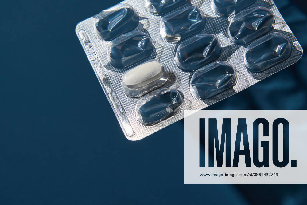Eine einzelne weiße Tablette, die teilweise in einer metallischen Blisterverpackung auf tiefblauem Hintergrund sitzt Single White Tablet Partially Seated In Metallic Blister Pack On Deep Blue Background With Reflective Highlights And Defined Shadows Under Controlled Studio Illumination For Medical Product Display. (License=RF)