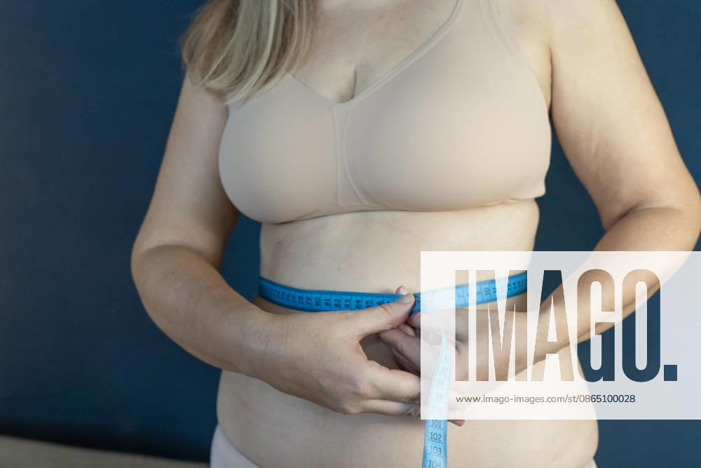 Frau, die ihren Taillenumfang mit einem Maßband misst, um den Fortschritt ihrer Diät zu überprüfen Woman measuring her waist with a blue tape measure, focusing on weight loss, body monitoring, and health goals (License=RF) ,model released, Symbolfoto