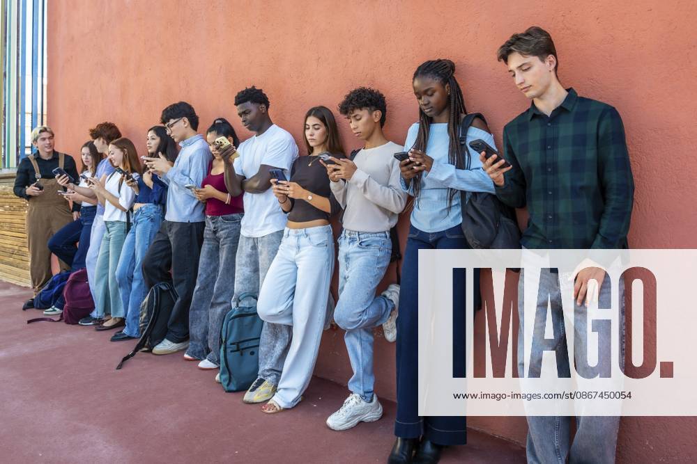 Vielfältige Gruppe von Teenagern der Generation Z, die in einer Reihe stehen, individuell in ihren Mobiltelefonen versunken sind und die Sucht nach sozialen Medien und digitaler Kommunikation symbolisieren Diverse group of gen z teenagers standing in a line, individually absorbed in their mobile phones, symbolizing social media addiction and digital communication