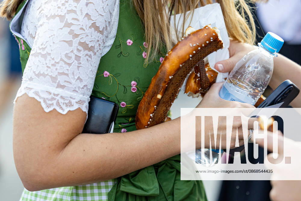 Oktoberfest 2026 in Munich, October 4, 2026: A female visitor wearing a dirndl holds a pretzel and a bottle of water on the festival grounds. The 191st Oktoberfest took place from September 19 to October 4, 2026, at the Theresienwiese. Munich’s Oktoberfest is one of the largest folk festivals in the world and attracts millions of v
