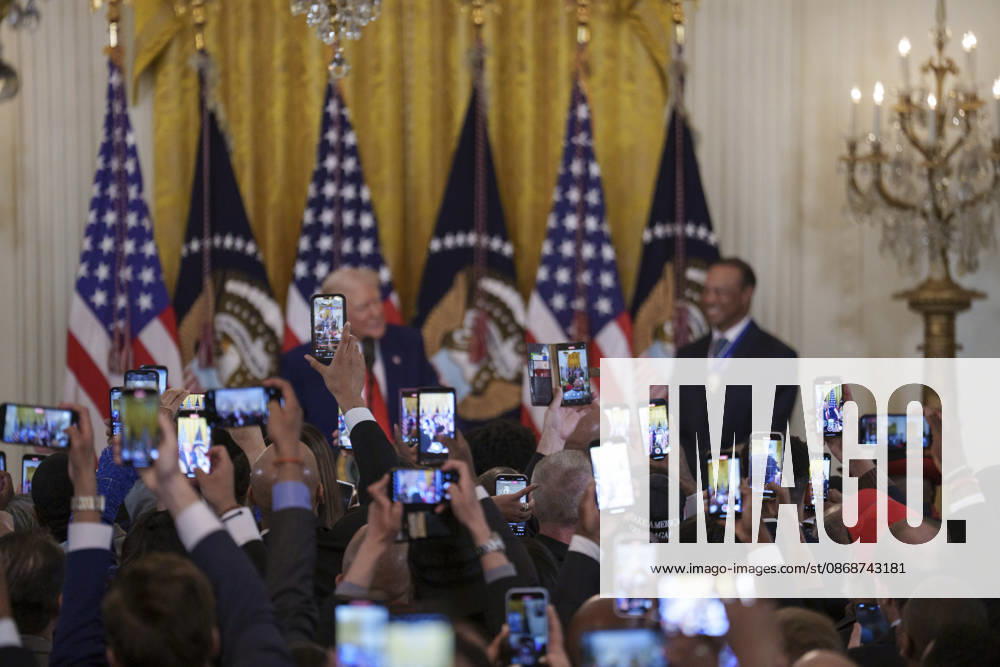 Guests take photos using their phones as U.S. President Donald Trump and golfer Tiger Woods appear at a reception honoring Black History Month in the East Room of the White House, February 20, 2025 in Washington, D.C. Trump introduced golfer Tiger Woods as a surprise guest at the reception in the East Room, where he praised Woods as one of the greatest athletes of all time. Washington United States of America - ZUMAp138 20261006_zaa_p138_018