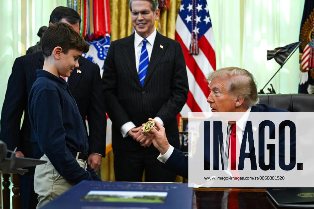 WASHINGTON, DC - OCT. 7: United States President Donald J Trump hands a challenge coin to a child during an announcement on Trump Accounts in the Oval Office of the White House in Washington, DC, USA, on Wednesday, October 7, 2026. Standing behind the President, from left to right: Frank J Bisignano, Commissioner, Social Security Administration (SSA); and US Secretary of the Treasury Scott Bessent.
