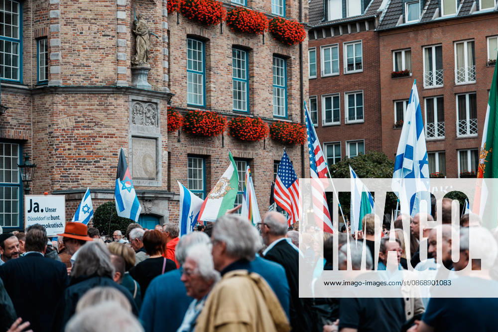 Rally in Düsseldorf marking the anniversary of Hamas’s terrorist attack on Israel on October 7, 2023, and protesting anti-Semitism; flags in front of City Hall, including a historic U.S. flag, as well as flags of Iran and Israel