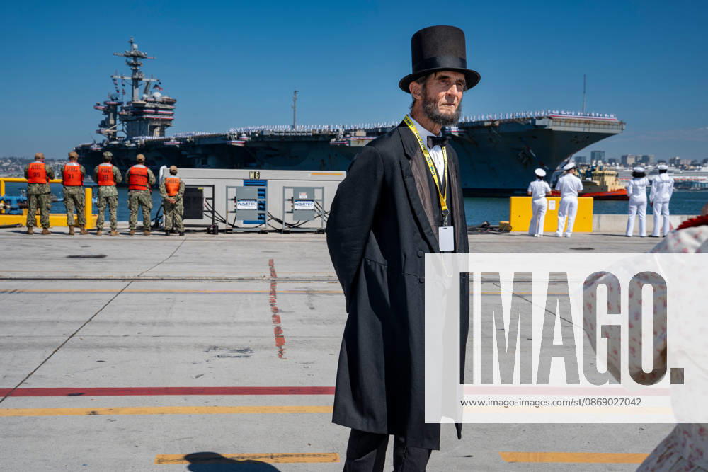 Robert Broski, an Abraham Lincoln presenter dressed in period attire, stands on the pier as the aircraft carrier USS Abraham Lincoln (CVN 72) returns to Naval Air Station North Island in Coronado, California, on October 8, 2026, following a deployment. Sailors and personnel gather along the waterfront as the carrier arrives. Coronado United States - ZUMAg374 20261008_znp_g374_020