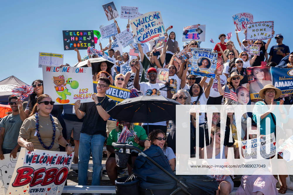 Family members and supporters cheer and hold handmade signs as the aircraft carrier USS Abraham Lincoln (CVN 72) returns to Naval Air Station North Island in Coronado, California, on October 8, 2026, following a deployment. The signs display personal messages welcoming sailors home, including Welcome Home Bebo and Welcome Home James. Coronado United States - ZUMAg374 20261008_znp_g374_021