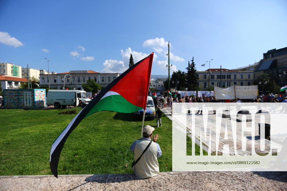 A demonstrator holding a Palestinian flag sits on a low wall as protesters gather nearby. Athens GREECE - ZUMAx103 20261010_zip_x103_008