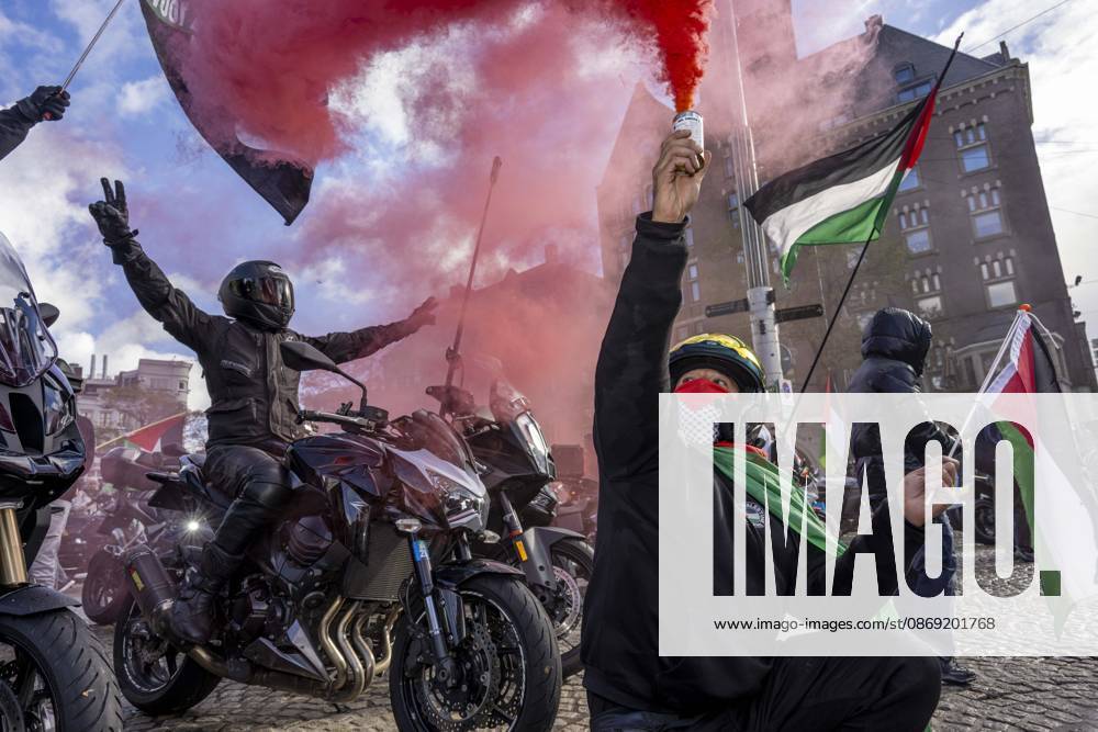 Amsterdam, Noord-Holland, The Netherlands: October 11, 2026, Amsterdam, Netherlands: A demonstrator crouches beside motorcycles and raises a canister emitting red smoke during a pro-Palestinian protest at Dam Square. A motorcyclist behind them raises both arms. Amsterdam The Netherlands - ZUMAl165 20261011_zip_l165_013