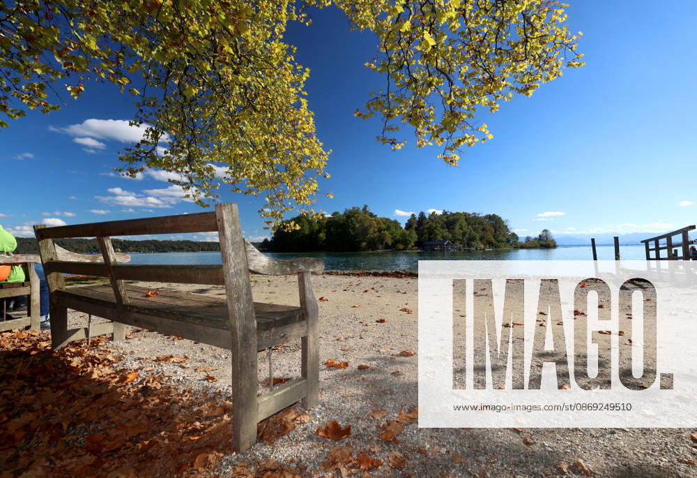 An autumn day in Feldafing, Feldafinger Park, Starnberg District. Here is a view of Lake Starnberg with Rose Island; in the foreground, a park bench, colorful trees, autumn foliage, deciduous trees, autumnal, play of colors, autumn leaves, autumn colors, leaf coloration, red, yellow, yellow foliage, natural spectacle, autumn scene, autumn impression, weather scene