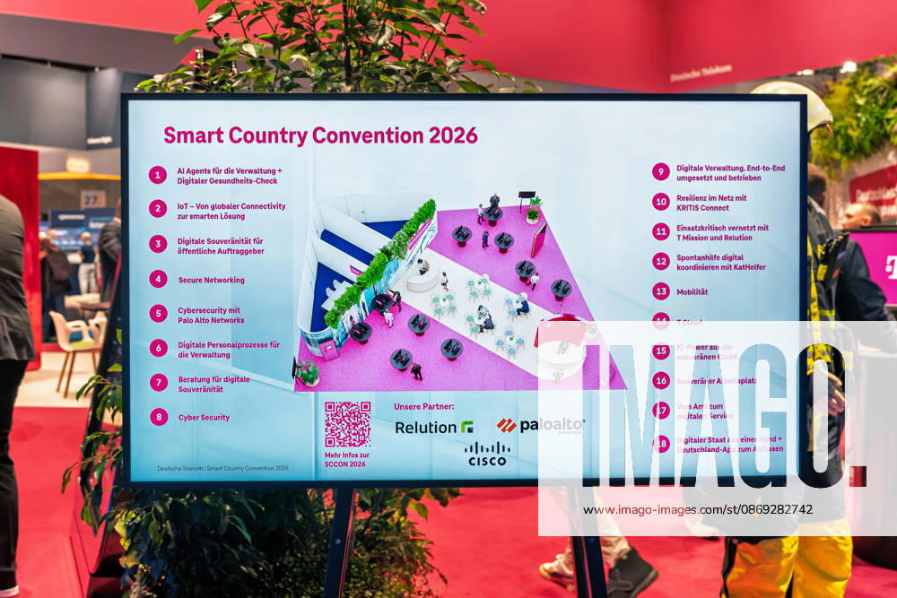 Berlin, 13.10.2026: Ein Bildschirm zeigt den Standplan der Deutschen Telekom auf der Smart Country Convention 2026 mit 18 Themeninseln, darunter KI-Agenten für die Verwaltung, digitale Souveränität für öffentliche Auftraggeber, Cybersecurity mit Palo Alto Networks, die T Cloud sowie die Deutschland-App; als Partner werden Relution, Palo Alto Networks und Cisco genannt. Rechts im Bild steht eine Person in Feuerwehr-Einsatzkleidung, passend zum Themenfeld einsatzkritischer Kommunikation für Behörden und Organisationen mit Sicherheitsaufgaben. Die Smart Country Convention (SCCON) ist die Kongressmesse für die Digitalisierung des öffentlichen Sektors und wird vom Digitalverband Bitkom gemeinsam mit der Messe Berlin veranstaltet. Vom 13
