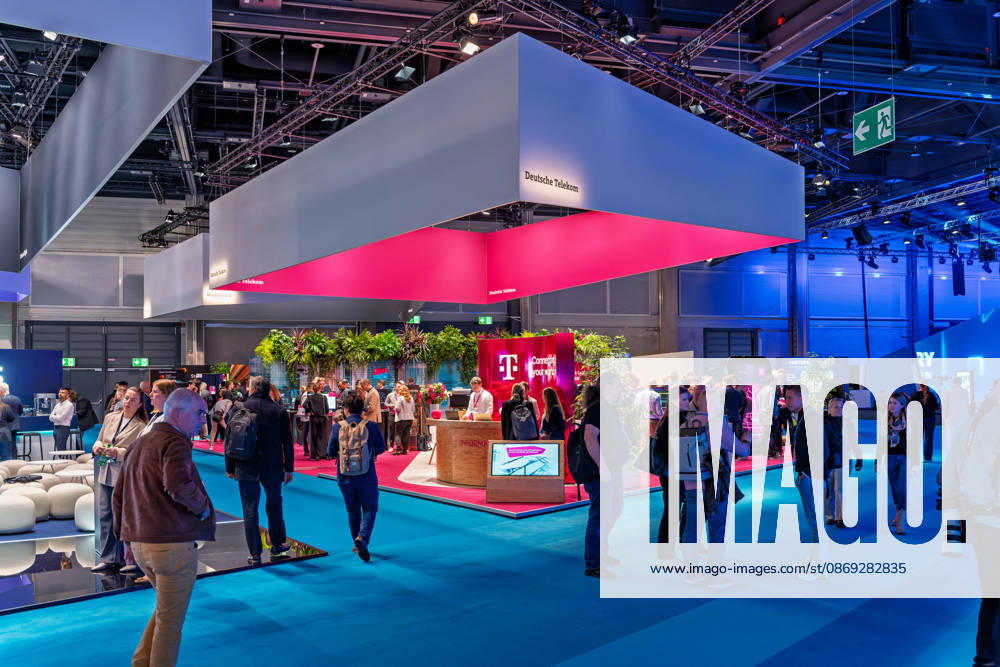 Berlin, 13.10.2026: Besucher gehen am Messestand der Deutschen Telekom auf der Smart Country Convention in der Halle hub27 vorbei, über dem ein großer, in Magenta beleuchteter Deckenaufbau schwebt. Der Konzern präsentiert dort auf 18 Themeninseln Lösungen für die öffentliche Verwaltung, darunter KI-Agenten, souveräne Cloud-Angebote, Cybersecurity und einsatzkritische Kommunikation für Behörden und Organisationen mit Sicherheitsaufgaben. Die Smart Country Convention (SCCON) ist die Kongressmesse für die Digitalisierung des öffentlichen Sektors und wird vom Digitalverband Bitkom gemeinsam mit der Messe Berlin veranstaltet. Vom 13. bis 15. Oktober 2026 treffen sich in der Halle hub27 Vertreter aus Bund, Ländern und Kommunen mit Unt