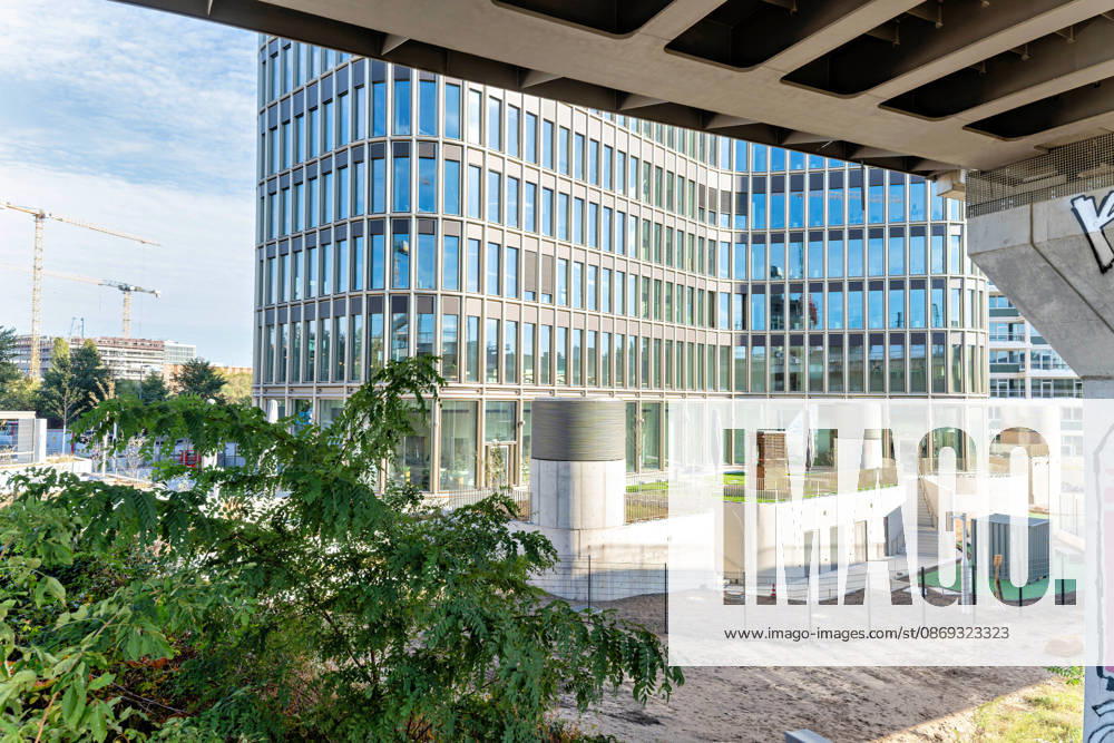Berlin, 13.10.2026: Blick unter einer Brücke hindurch auf den Sockel des neuen DKB-Campus in der Europacity in Berlin-Mitte mit begrünten Terrassen; links drehen sich Baukräne im weiter wachsenden Stadtquartier. Die Deutsche Kreditbank AG (DKB) hat ihren neuen Hauptsitz heute offiziell eröffnet. Der von Kleihues + Kleihues entworfene, rund 82 Meter hohe Komplex besteht aus drei Gebäudeteilen mit fünf, elf und 19 Geschossen und rund 35.000 Quadratmetern Mietfläche; entwickelt wurde er von der CA Immo unter dem Projektnamen Upbeat. Rund 2.600 Mitarbeitende des DKB-Konzerns, die bislang auf mehrere Berliner Standorte verteilt waren, arbeiten nun gemeinsam im Campus. Die DKB ist Exklusivmieterin und hat einen Mietvertrag über 15 J