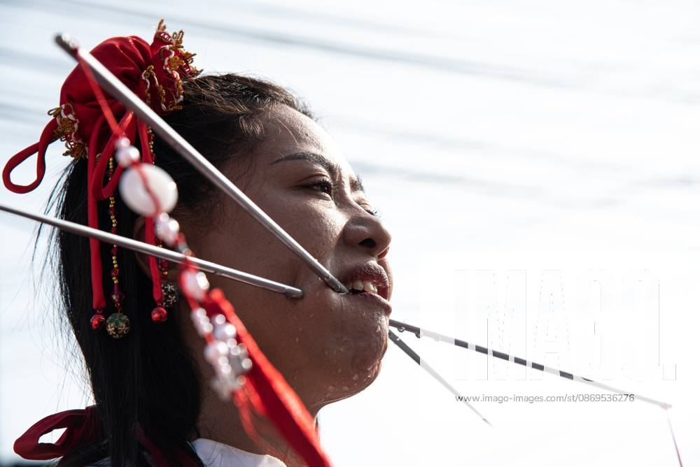 A devotee with a skewer piercing her cheek participates in a street procession during the Vegetarian Festival..The annual Vegetarian Festival is held in Bangkok and many parts of southern Thailand, including Trang, Phang Nga, and Phuket, where worshippers refrain from eating animal products over the nine days, coinciding with the celebration of the Nine Emperor Gods. Trang Thailand - ZUMAs197 20261015_aaa_s197_019