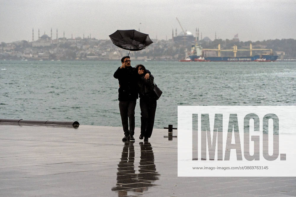 A coupleâ€⠢s umbrella blows away by wind as they walk near a waterfront in Istanbul, Turkey. Istanbul faces another round of heavy rain after floods that left five people dead, with orange alerts in place and downpours expected to intensify, according to To¼rkiye Today. Istanbul Turkey - ZUMAz174 20261017_zip_z174_002