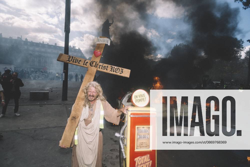 A man dressed as Jesus carries a cross reading Vive le Christ Roi in front of a burning car at Place de la Republique in Paris. A national day of mobilization against the high cost of living took place across France on October 17, 2026, joined by Yellow Vests, high school and university students, trade unions, farmers and taxi drivers. In Paris, clashes with police broke out at Place de la Republique even before the march, due to leave at 2 p.m. for Place de Clichy, set off, and the police prefecture banned demonstrations in several areas of the city citing serious risks of public disorder. Paris France - ZUMAs392 20261017_zip_s392_027