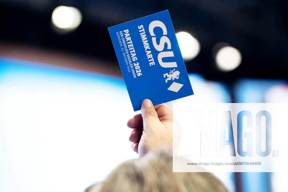 The 2026 party convention of the CSU (Christian Social Union) at the Munich Trade Fair Center. A hand holds a CSU voting card aloft; voting, cast a vote, vote, casting a vote