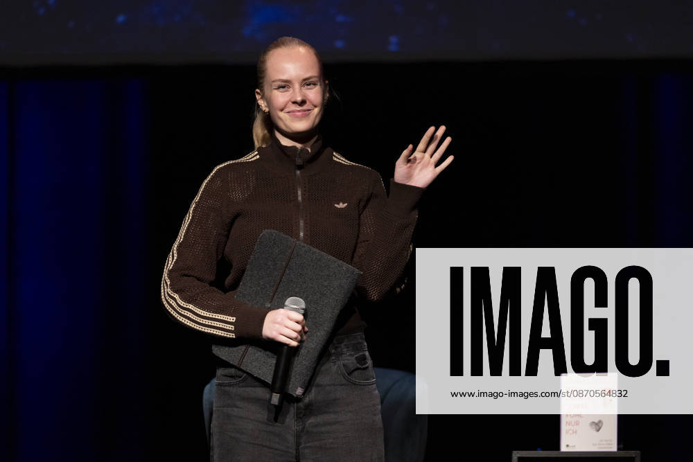 Poetry artist and author Clara LOESEL LÖSEL waves and smiles at the audience during her reading—a preview show for her new book, *Ich dachte, sowas fühle nur ich*—standing, single frame, single photo, at the Theater am Tanzbrunnen, Cologne, on October 23, 2026