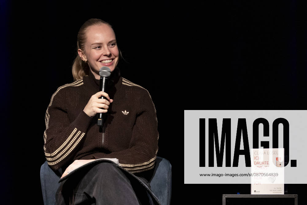 Poetry artist and author Clara LOESEL LÖSEL smiling, laughing, during her reading—a preview event for her new book, *Ich dachte, sowas fühle nur ich*—seated, holding a microphone; single frame, single photo, at the Theater am Tanzbrunnen, Cologne, on October 23, 2026