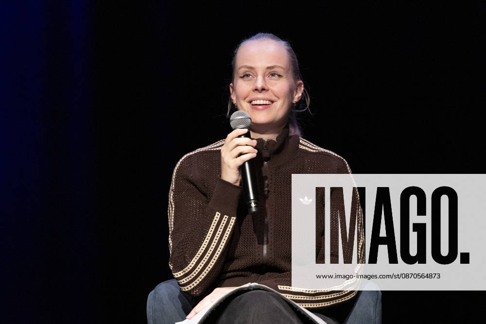 Poetry artist and author Clara LOESEL LÖSEL laughing during her reading, a preview show for her new book *Ich dachte, sowas fühle nur ich* (I Thought I Was the Only One Who Felt That Way), seated with a microphone; single frame, single photo, at the Theater am Tanzbrunnen, Cologne, on October 23, 2026