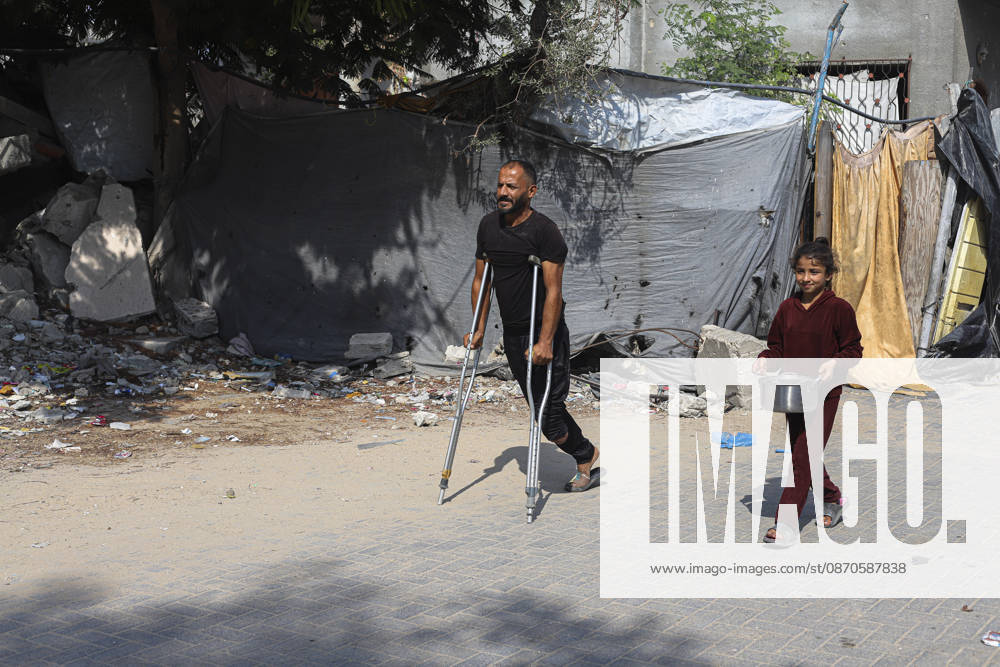 Gaza Palestinians Food Shortages 2026 A Palestinian man using crutches walks with a young girl carrying a metal cooking pot along a damaged street in Jabalia Refugee Camp, northern Gaza Strip, Palestine, on October 24, 2026. The UN says widespread damage, displacement and food shortages have left families across Gaza heavily dependent on humanitarian assistance, with food distributions reduced in October amid funding constraints. Jabalia Gaza Strip Palestinian Territories