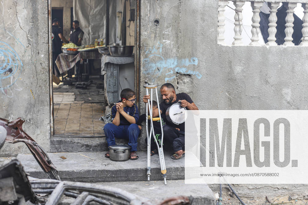 Gaza Palestinians Food Shortages 2026 A Palestinian man using crutches sits outside a damaged home beside children and cooking pots in Jabalia Refugee Camp, northern Gaza Strip, Palestine, on October 24, 2026. The UN says widespread damage, displacement and food shortages have left families across Gaza heavily dependent on humanitarian assistance, with food distributions reduced in October amid funding constraints. Jabalia Gaza Strip Palestinian Territories