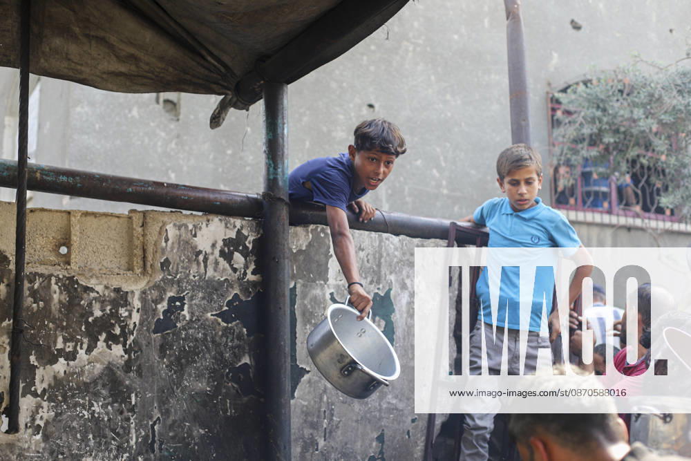 Gaza Palestinians Food Shortages 2026 A Palestinian boy carrying a cooking pot leans over a barrier beside a crowded food distribution point in Jabalia Refugee Camp, northern Gaza Strip, Palestine, on October 24, 2026. Community kitchens remain a key source of food in Gaza, where UN humanitarian agencies reported cuts to cooked-meal distributions in October because of funding shortages. Jabalia Gaza Strip Palestinian Territories