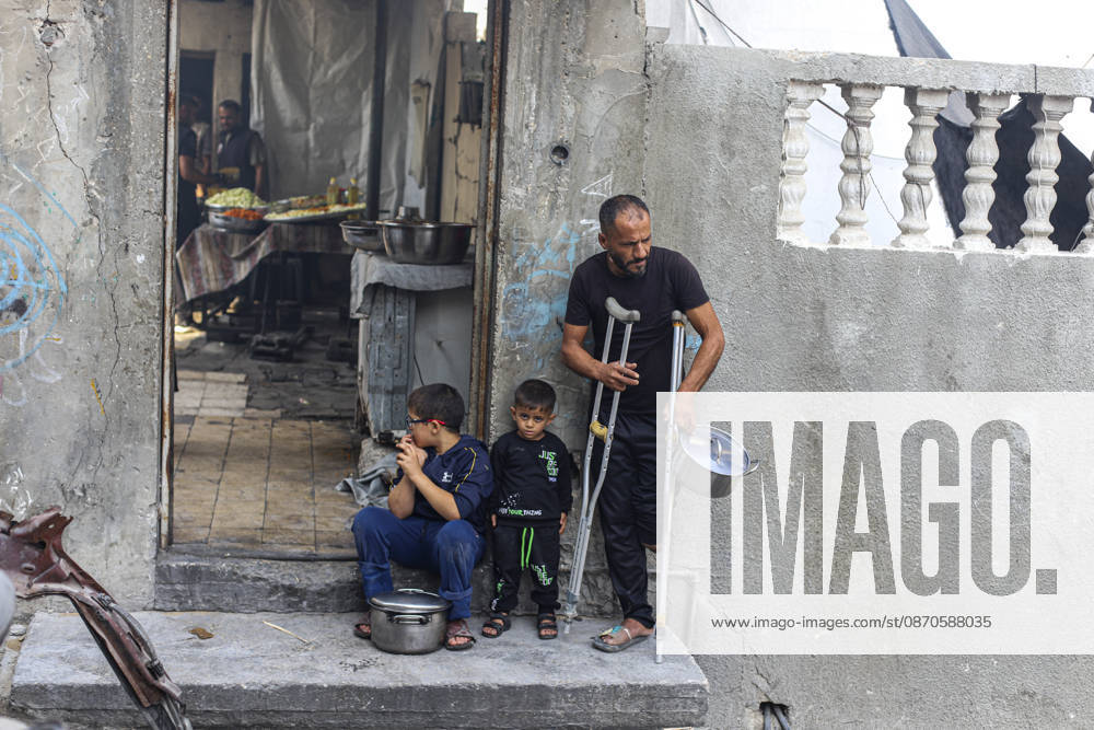 Gaza Palestinians Food Shortages 2026 A Palestinian man using crutches stands with children outside a damaged home, holding an empty cooking pot in Jabalia Refugee Camp, northern Gaza Strip, Palestine, on October 24, 2026. The UN says widespread damage, displacement and food shortages have left families across Gaza heavily dependent on humanitarian assistance, with food distributions reduced in October amid funding constraints. Jabalia Gaza Strip Palestinian Territories