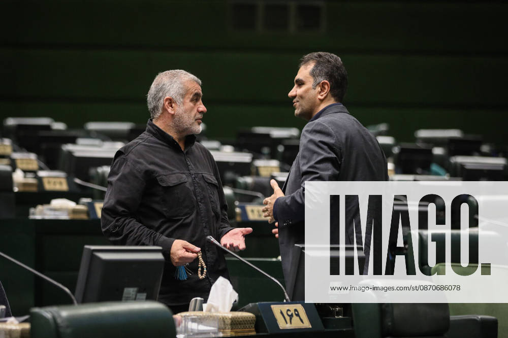 A gray-bearded lawmaker holds a document and gestures while talking to a suited colleague next to his desk at the Islamic Consultative Assembly in Tehran, Iran, on October 25, 2026. Parliamentary reports said more than two-thirds of lawmakers joined the October 25 open sitting of the Islamic Consultative Assembly, attending either in person or remotely. Tehran Iran - ZUMAi98_ 20261025_zih_i98_076