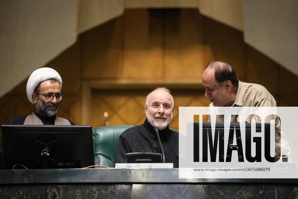 Mohammad Bagher Ghalibaf sits at the presiding desk between a turbaned cleric and a man leaning over a monitor at the Islamic Consultative Assembly in Tehran, Iran, on October 25, 2026. Parliamentary reports said more than two-thirds of lawmakers joined the October 25 open sitting of the Islamic Consultative Assembly, attending either in person or remotely. Tehran Iran - ZUMAi98_ 20261025_zih_i98_077