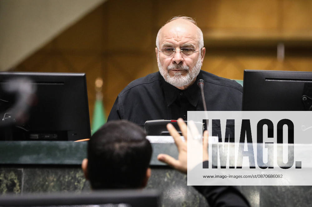 Mohammad Bagher Ghalibaf sits between two computer monitors while a raised hand appears in the foreground at the Islamic Consultative Assembly in Tehran, Iran, on October 25, 2026. The Iranian parliament held a hybrid open sitting, with some lawmakers attending in the Tehran chamber and others participating remotely, according to parliamentary reports. Tehran Iran - ZUMAi98_ 20261025_zih_i98_080