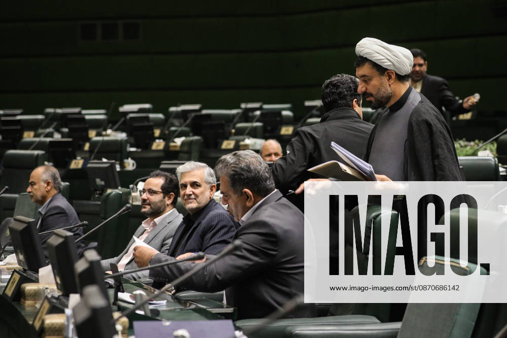 A white-turbaned cleric holding papers stands beside a row of seated lawmakers and desk monitors at the Islamic Consultative Assembly in Tehran, Iran, on October 25, 2026. Parliamentary reports said more than two-thirds of lawmakers joined the October 25 open sitting of the Islamic Consultative Assembly, attending either in person or remotely. Tehran Iran - ZUMAi98_ 20261025_zih_i98_093