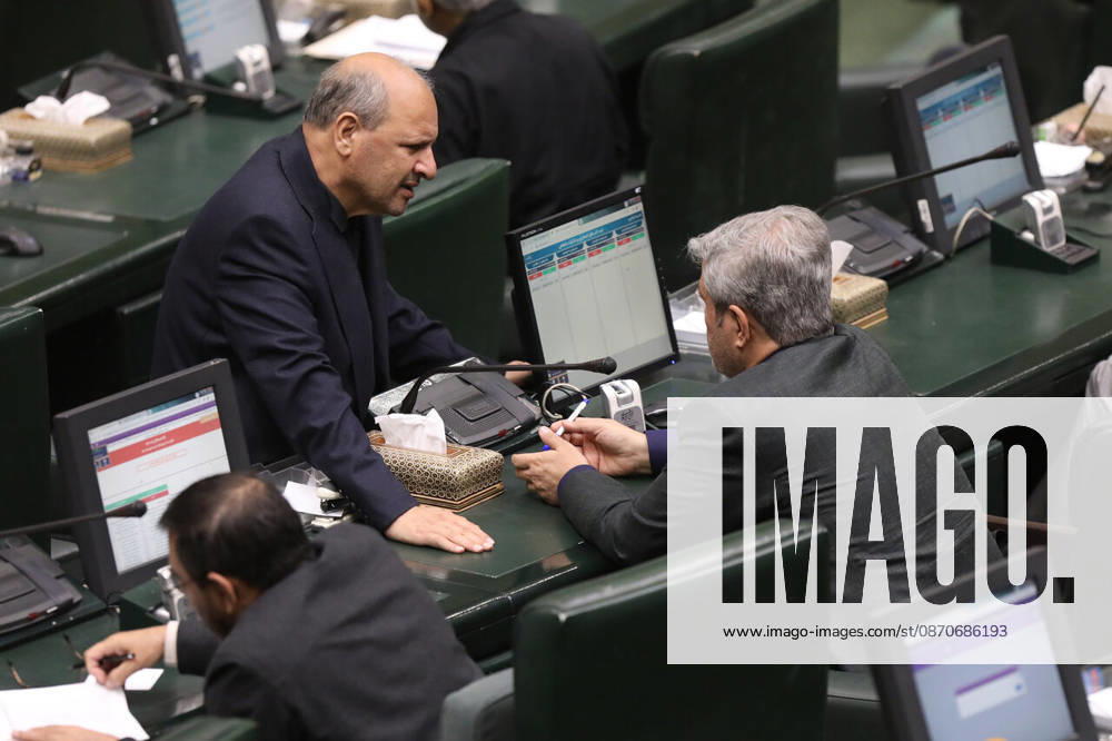 A gray-haired man leans forward across the green parliamentary seats to speak to another seated lawmaker at the Islamic Consultative Assembly in Tehran, Iran, on October 25, 2026. The Iranian parliament held a hybrid open sitting, with some lawmakers attending in the Tehran chamber and others participating remotely, according to parliamentary reports. Tehran Iran - ZUMAi98_ 20261025_zih_i98_113