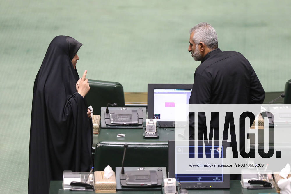 A woman in a black chador raises her index finger while speaking to a gray-haired man beside parliament seating at the Islamic Consultative Assembly in Tehran, Iran, on October 25, 2026. Parliamentary reports said more than two-thirds of lawmakers joined the October 25 open sitting of the Islamic Consultative Assembly, attending either in person or remotely. Tehran Iran - ZUMAi98_ 20261025_zih_i98_125