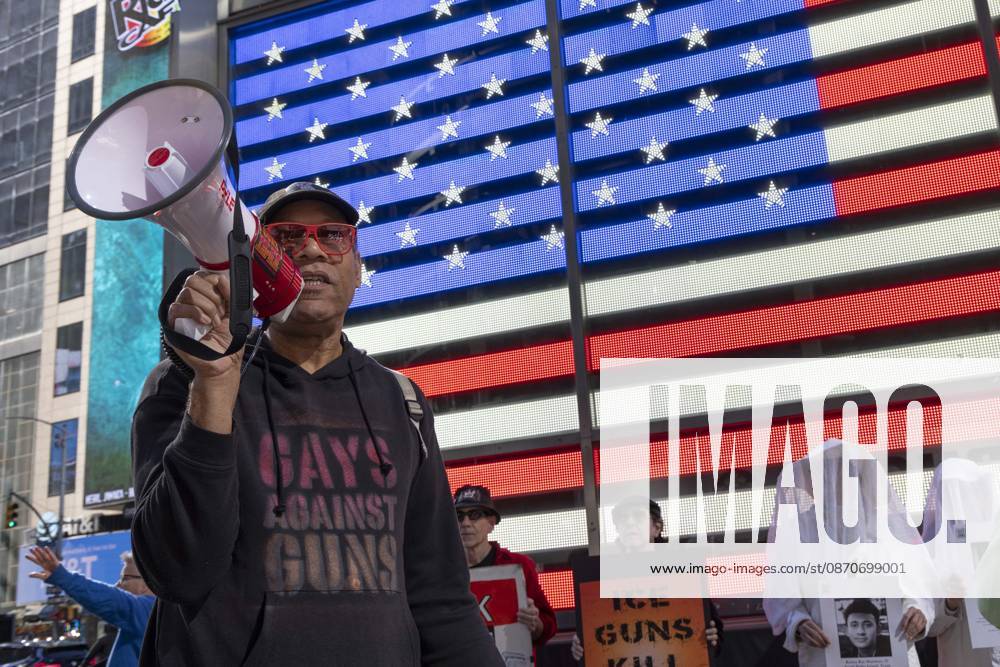 JAY W. WALKER, President of Gays Against Guns leads chants at a demonstration under the Times Square US Army Recruiting Station LED American flag to denounce U.S. Immigration and Customs Enforcement (ICE) and President Trump s immigrant detention and mass deportation policies. People dressed in white shrouds are Human Beings, memorializing people killed by gun violence from Federal immigration agents by holding signs with their images and names. New York USA - ZUMAr174 20261025_znp_r174_011