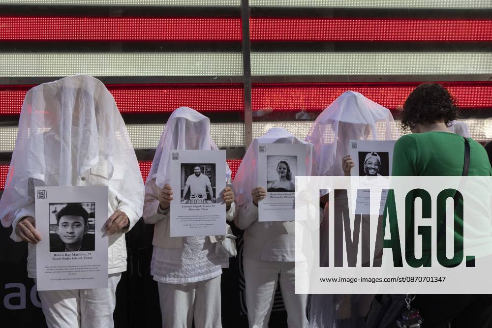 A passerby stops to observe people dressed in white shrouds, Human Beings, memorializing those killed by gun violence from Federal immigration agents by holding signs with the images and names of Ruben Ray Martinez Lorenzo Salgado Araujo Renee Nicole Good Keith Porter Jr. Demonstrators with the anti-gun violence organization Gays Against Guns protest under the Times Square US Army Recruiting Station LED American flag to denounce U.S. Immigration and Customs Enforcement (ICE,) President Trump s immigrant detention and mass deportation policies. New York USA - ZUMAr174 20261025_znp_r174_012