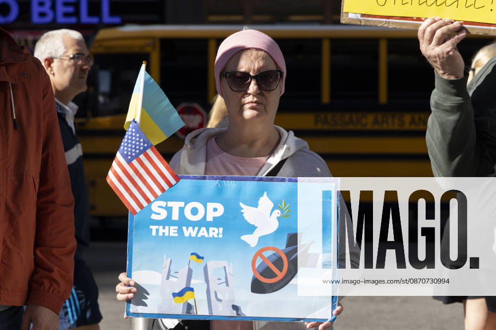 A demonstrator holding Ukrainian and American flags and a sign that reads STOP THE WAR! with images of a dove and a red circle slash over a bomb stands with a group of protesters in Times Square. New York USA - ZUMAr174 20261025_znp_r174_028