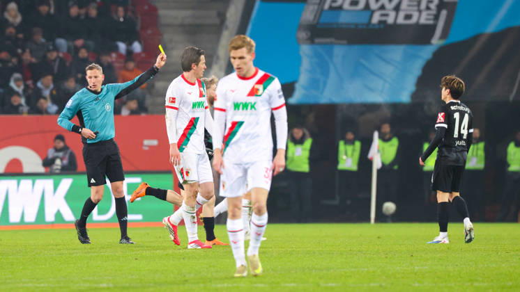 Martin Petersen Referee shows Yuito Suzuki 14, SC Freiburg , the yellow card at the match between FC Augsburg v SC Freiburg, Football, Men, Bundesliga, 2025 2026, Matchday 18 on 18 01 2026 in Augsburg, WWK Arena DFL and DFB regulations prohibit any use of photographs as image sequences and or quasi video Bayern Germany