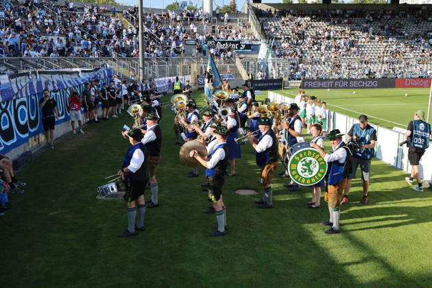 Soccer, Men s, Bavarian Regional League, 2026–2027 Season, TSV 1860 Munich vs. FC Augsburg II, Grünwalder Stadium: The Sechzger Musikanten, a brass band affiliated with TSV 1860 Munich, performing in front of the West Stand