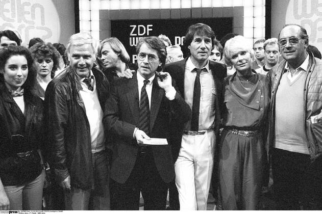 Wetten, dass...? -Finale- 10 83 stroe Isabel Varell, Joachim Fuchsberger, Volker Lechtenbrink (hinten), Frank Elstner, Udo Jürgens und Elke Sommer (v.li.) am 15.10.1983 in Wetten, dass...? (ZDF) aus der Rheingoldhalle in Mainz Deutschland deutsch Mann Schauspiel Schauspieler Moderator Moderation Quizmaster Talkmaster Showmaster Autor Schriftsteller Kino Film TV Fernsehen grauhaarig weißhaarig kurzhaarig seriös Sakko Jackett Krawatte Sängerin Sänger Gesang Musiker Musikerin Musik Schauspielerin Schlußbild Fernsehstudio Studio Fernsehkulisse Kulisse Halle Querformat quer halb stehend stehen lächelnd Lächeln gestikulierend gestikulieren Gestik umarmend umarmen Blacky sw s w schwarzweiß rechts vermutlich Saalkandidat Wolfgang Zimmer