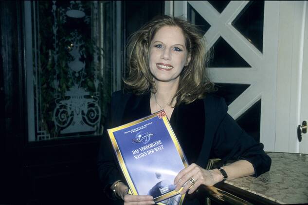 Penny McLean (Sängerin) 02 97 kück Frau Gesang Musik rothaarig langhaarig Locken seriös Blazer schwarz Schmuck Kette stehend Buch haltend Titel Logo halb quer aufstützend lächelnd