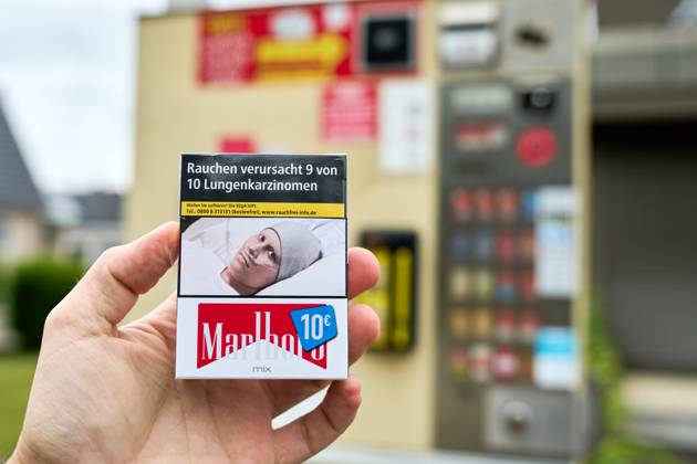 Stettenhofen, Bavaria, Germany - May 28, 2024: Hand holds a pack of Marlboro cigarettes costing 10 euros in front of a cigarette machine. There is a warning on the cigarettes: Smoking causes 9 out of 10 lung cancers