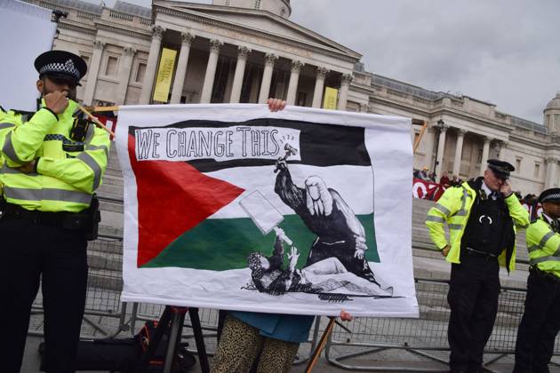 October 4, 2025, London, United Kingdom: A protester holds a banner with a Palestinian flag and the Bansky artwork depicting a judge hitting a demonstrator with a gavel during the demonstration in Trafalgar Square. Hundreds of people gathered to show support for the activist group Palestine Action, which has been banned under anti-terrorism law, and demanded that the ban is lifted. London United Kingdom - ZUMAs197 20251004_aaa_s197_248 Copyright: xVukxValcicx